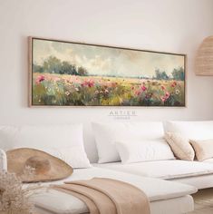 a painting hanging above a couch in a living room with pillows and blankets on it