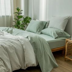 a bed with green sheets and pillows in a bedroom next to a plant on the floor