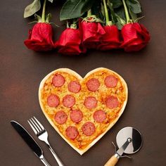 a heart shaped pizza sitting on top of a table next to utensils and roses