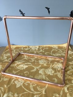 a metal frame sitting on top of a gold fabric covered tablecloth with birds flying above it