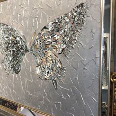 a butterfly is shown on a silver and black wall hanging in a frame with gold trimmings