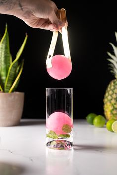 a person is pouring water into a glass filled with pink liquid and limes on the side