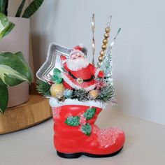 a santa clause boot with christmas decorations on it sitting next to a potted plant