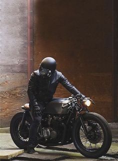 a man wearing a black leather jacket and helmet sitting on a parked motorcycle in front of a building