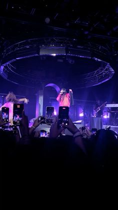 a man standing on top of a stage with his arms in the air and people holding up their cell phones