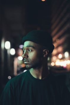 a man standing in front of a building at night wearing a black shirt and beanie