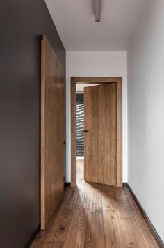 an empty hallway with wooden doors and hard wood flooring on one side, looking into the other