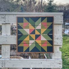 a wooden bench with a patchwork quilt hanging on it's back end and grass in the background