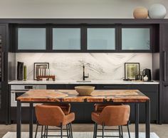 a kitchen with black cabinets and marble counter tops, along with two brown chairs at the table