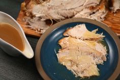 a blue plate topped with sliced meat next to a cup of gravy and a cutting board