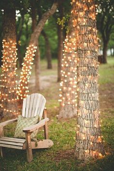 a wooden chair sitting in the grass next to a tree with lights strung all over it