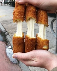 a person holding up four pieces of food in their hands on the sidewalk near a street