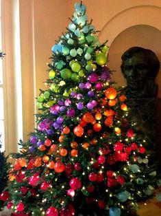 a brightly colored christmas tree in the middle of a room with a busturine behind it