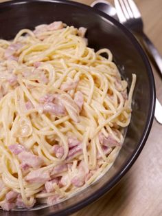 a bowl filled with pasta and ham on top of a wooden table