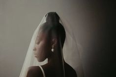 a woman wearing a veil and earrings standing in front of a white wall with her eyes closed