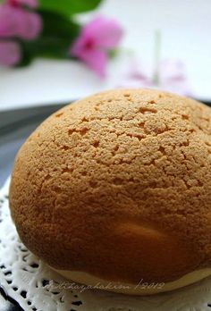 a round cake sitting on top of a doily next to pink flowers in the background