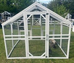 a white chicken coop in the grass with a dog inside and an open door on one side