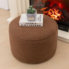 a round ottoman with a cactus on it next to a fire place and book sitting on top