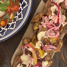 a wooden tray topped with meat and veggies next to a bowl of salad