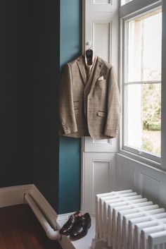 a suit hanging on the wall next to a radiator with shoes underneath it