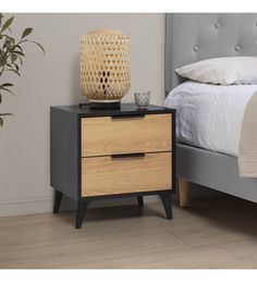 a nightstand with two drawers and a lamp on top of it next to a bed