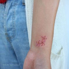 a woman's arm with a small pink flower tattoo on the left side of her wrist