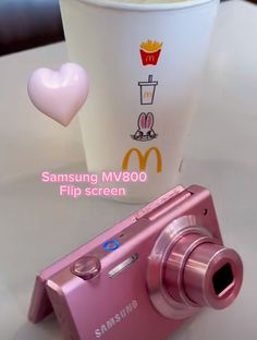 a pink camera sitting on top of a table next to a cup