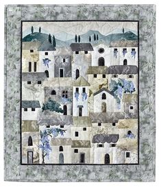 a quilted wall hanging with buildings and trees in the background on a white surface