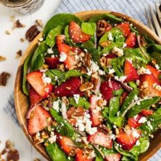 a salad with strawberries and green beans in a wooden bowl on a white table