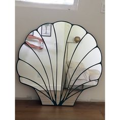 an art deco mirror in the shape of a sea shell on a wooden floor next to a window