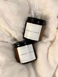 two jars of orange and clove candles on a white furnishing material,