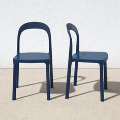 two blue chairs sitting next to each other in front of a white wall and cement floor