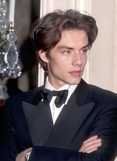 a young man in a tuxedo poses for the camera with his arms crossed