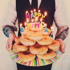 a man holding a birthday cake with donuts on it and lit candles in the middle