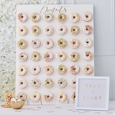 a white table topped with donuts next to a sign and vase filled with flowers