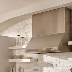 a stainless steel hood in a kitchen with white brick walls and shelves on either side