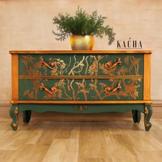 a green and gold painted dresser sitting on top of a hard wood floor next to a potted plant