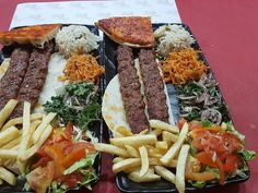 two black trays filled with different types of food on top of a red table