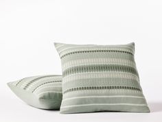 two pillows sitting next to each other on top of a white surface with green and gray stripes