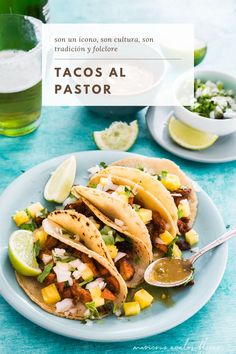 three tacos on a plate with limes and cilantro in the background