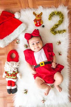 a baby dressed up as santa clause laying on a rug next to other christmas decorations