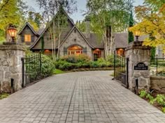 a stone driveway leading to a house with an iron gate and brick walkway that leads into the front yard