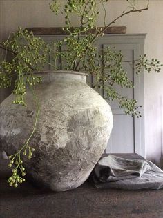 a large vase sitting on top of a wooden table next to a plant in it