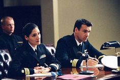 two pilots sitting at a table with microphones in front of them and another man standing behind them