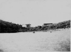 an old black and white photo of people in boats on the water near a hill