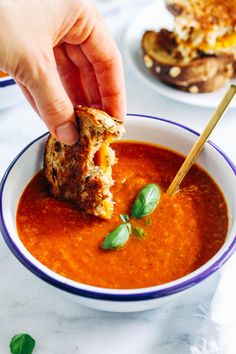 a person dipping something into a bowl of tomato soup with bread on the other side