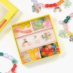 a yellow box filled with lots of different colored beads and jewelry on top of a white table