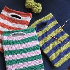 three knitted bags sitting next to each other on a blue surface with knitting needles