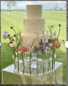 a wedding cake with flowers in the middle on top of it and an image of a field behind it