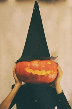 a woman holding up a pumpkin with a witches hat on her head